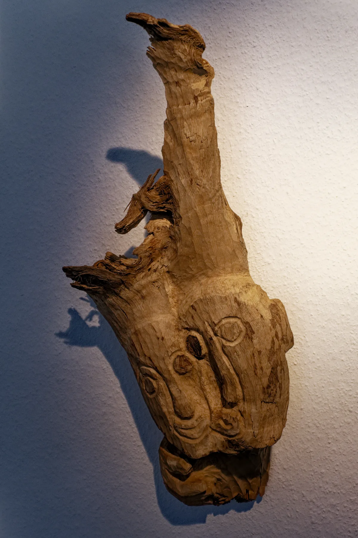 »Zwei Liebende« – ineinander verschmolzene Holzskulptur mit zwei Gesichtern Zwei Liebende: ineinander verschmolzene Holzskulptur mit zwei Gesichtern an der Praxiswand